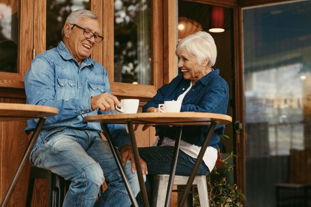 elderly couple laughing and drinking coffee outside a restaurant
