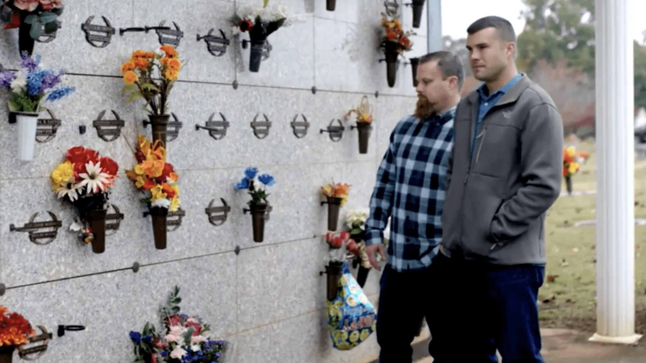 two men standing in front of a wall with bouquets hanging