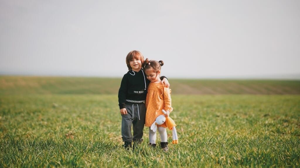 little boy hugging little girl in an open field