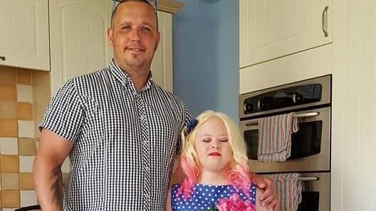 man in a striped shirt standing with a teen girl in a blue dress