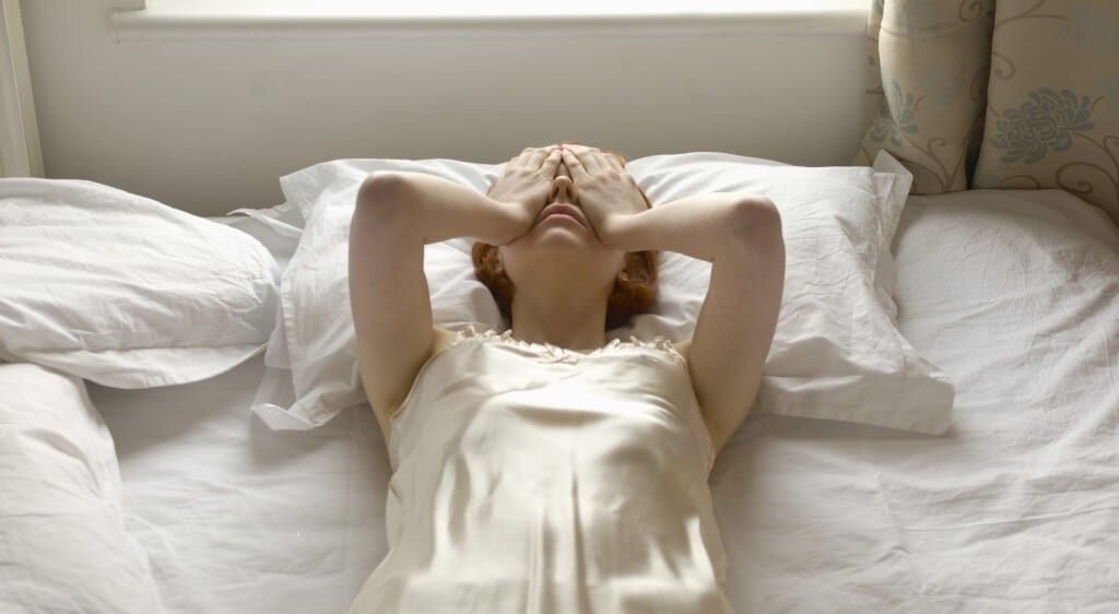 woman on bed with hands over eyes