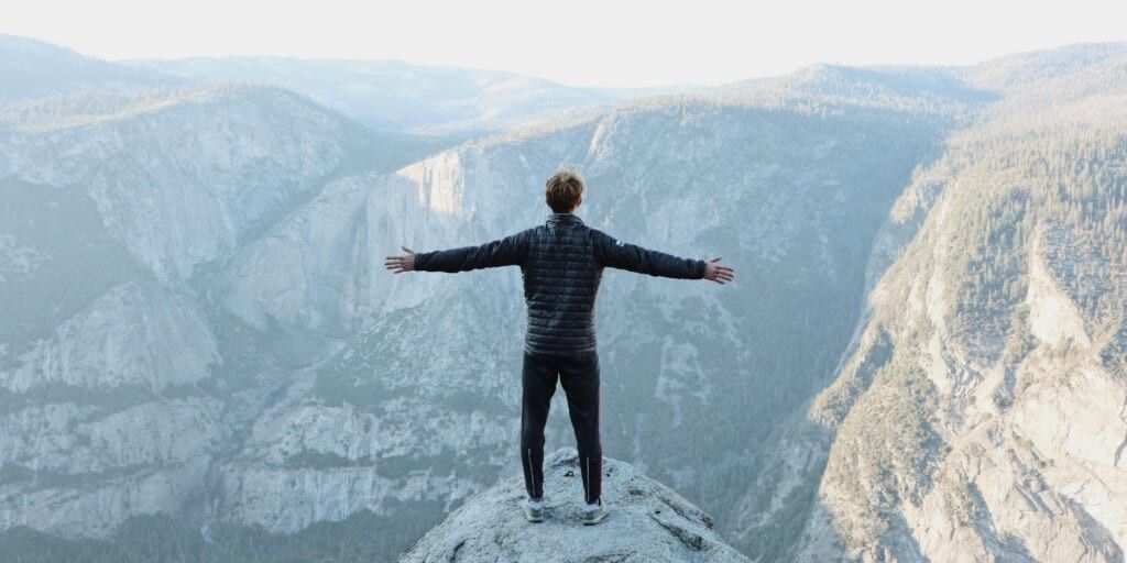 Man standing atop a mountain with arms wide open overlooking mountains by Jason Hogan on Unsplash