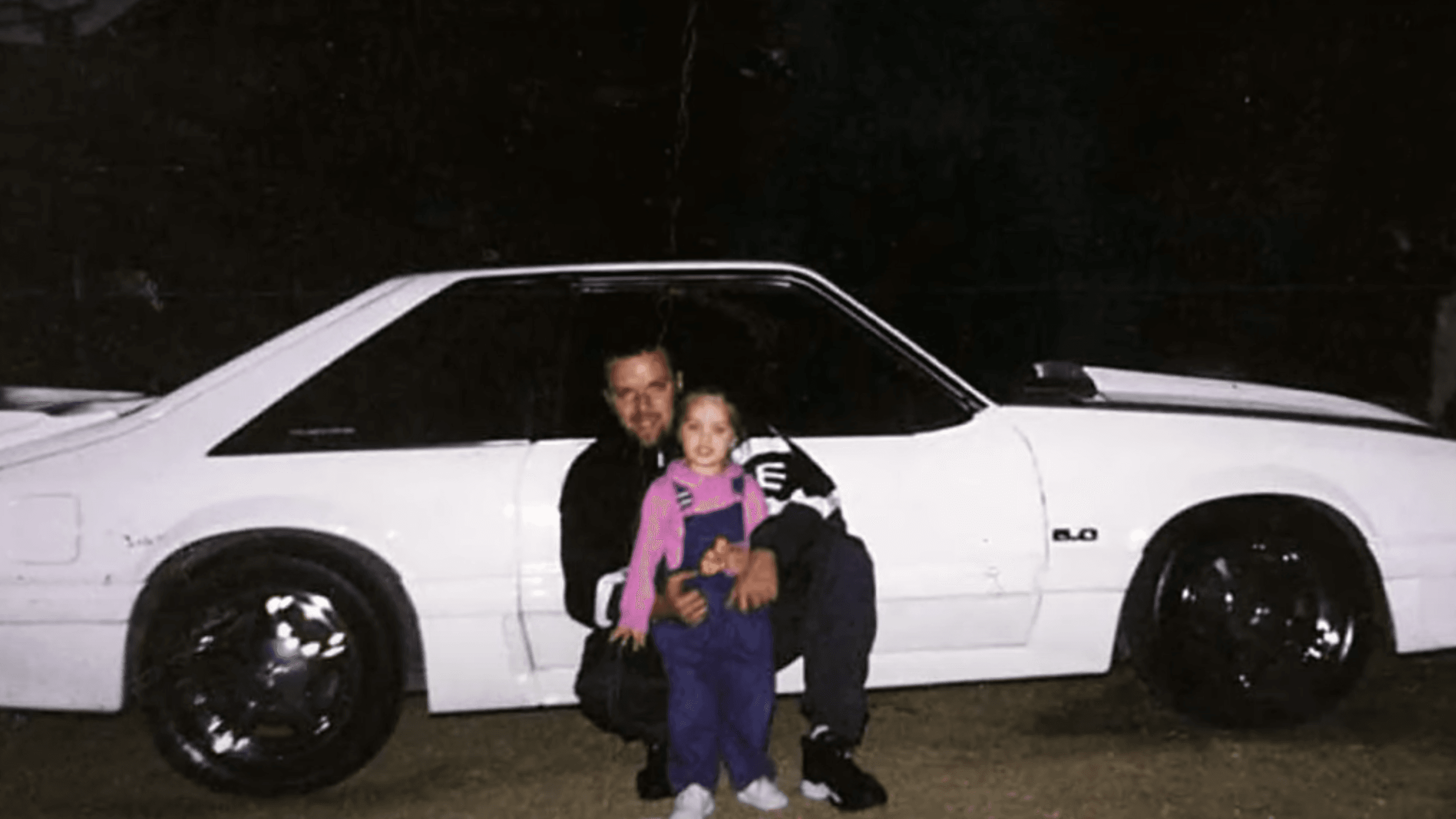 man with a little girl in front of a white car
