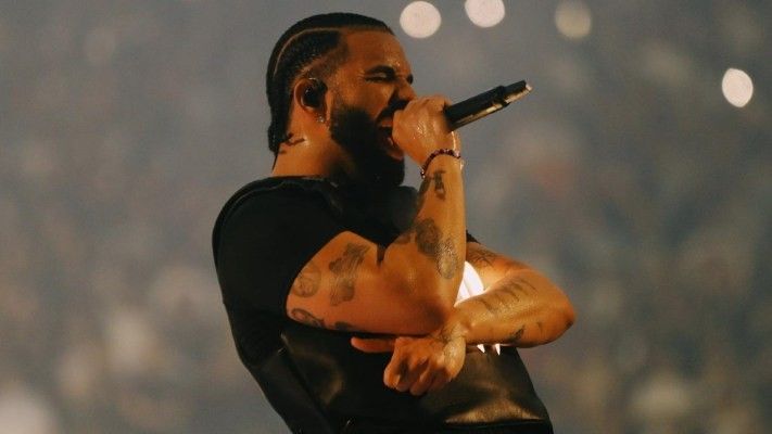 Drake holding a microphone on stage and singing.