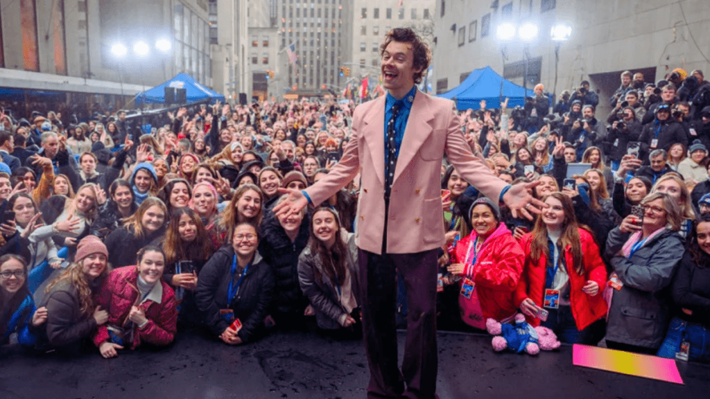Harry Styles smiling in front of a crowd of fans in New York City.