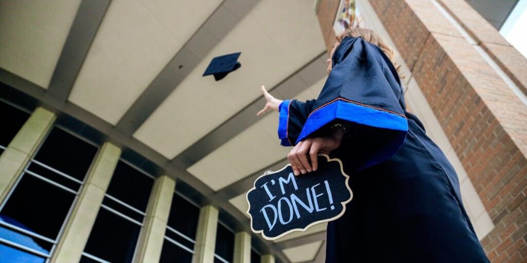 Graduate throwing cap in the air holding sign saying I