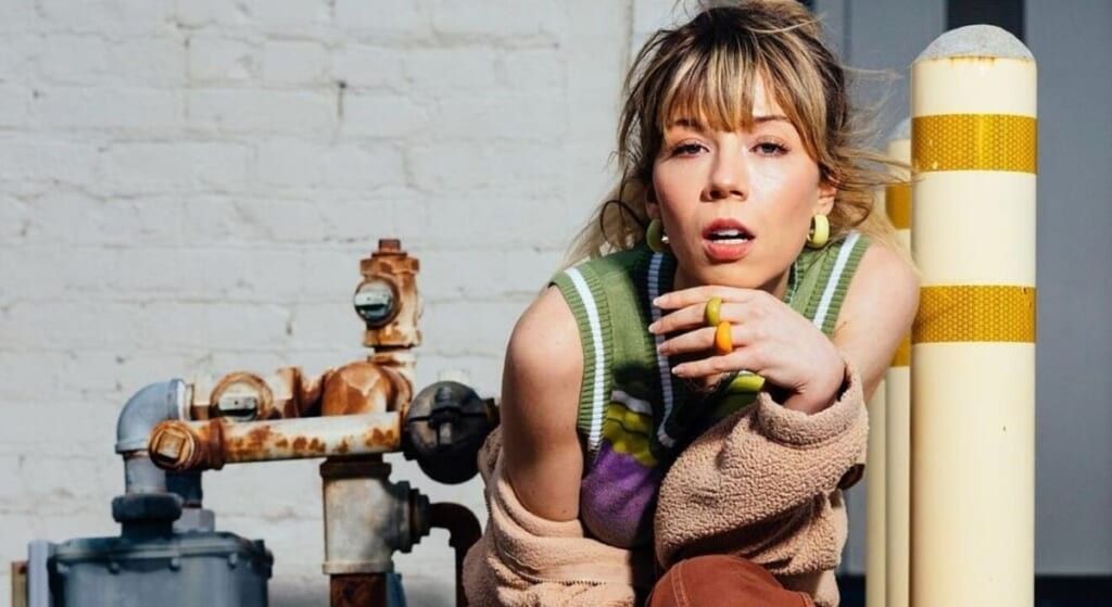 Jennette McCurdy  crouched down with sweater hanging off her shoulders.