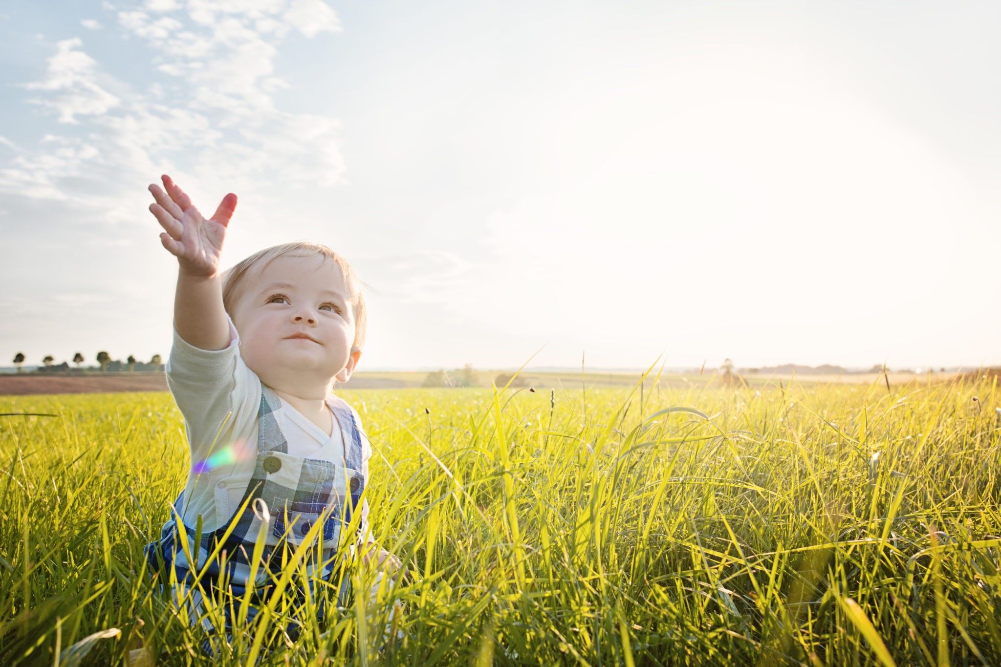 Baby sitting in grass reaching to the sky 1