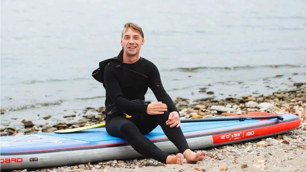man in a black wet suit sitting on a paddleboard at the beach