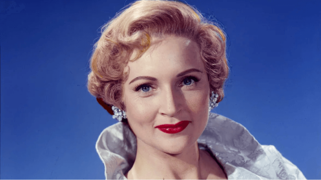 An archival image of a young Betty White wearing earrings and red lipstick.