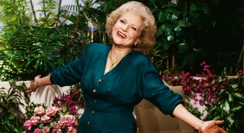 Betty White in green dress, arms spread out in the Golden Girls backyard
