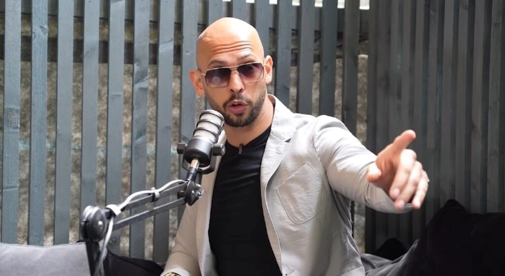 Andrew Tate during an interview wearing grey jacket and pointing at the camera.