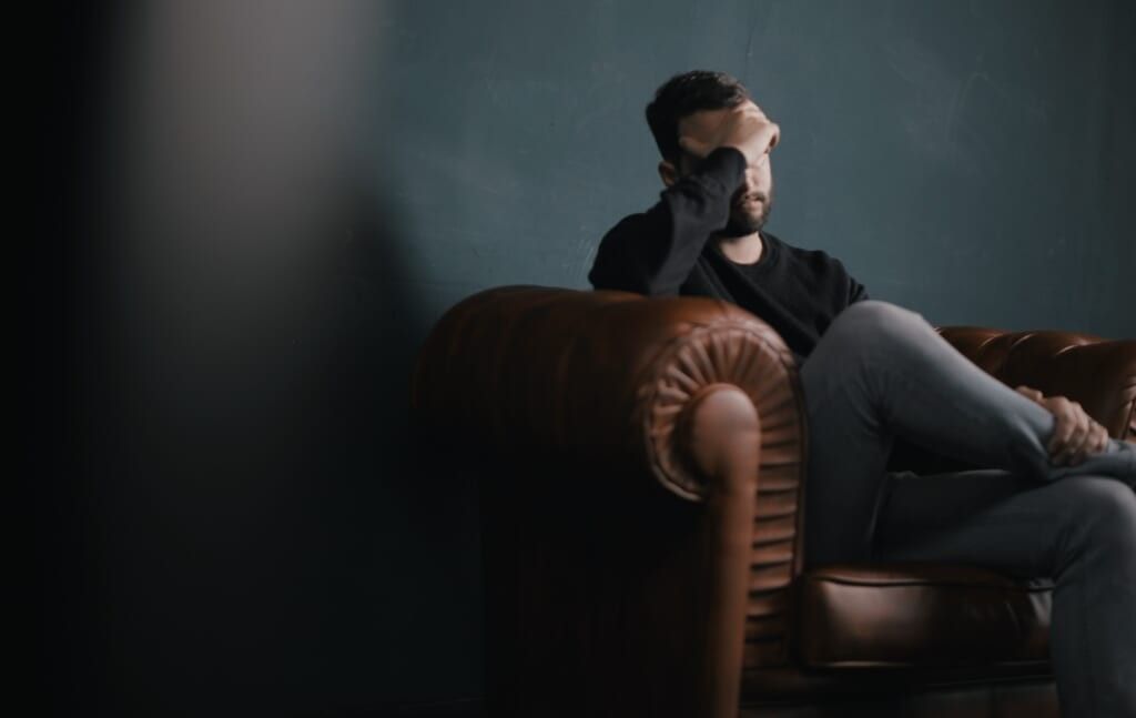 depressed young man sits on couch holding face