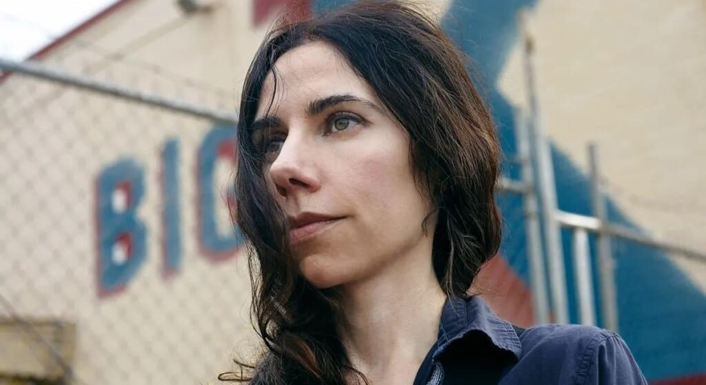 Musician PJ Harvery outside in front of a chain link fence