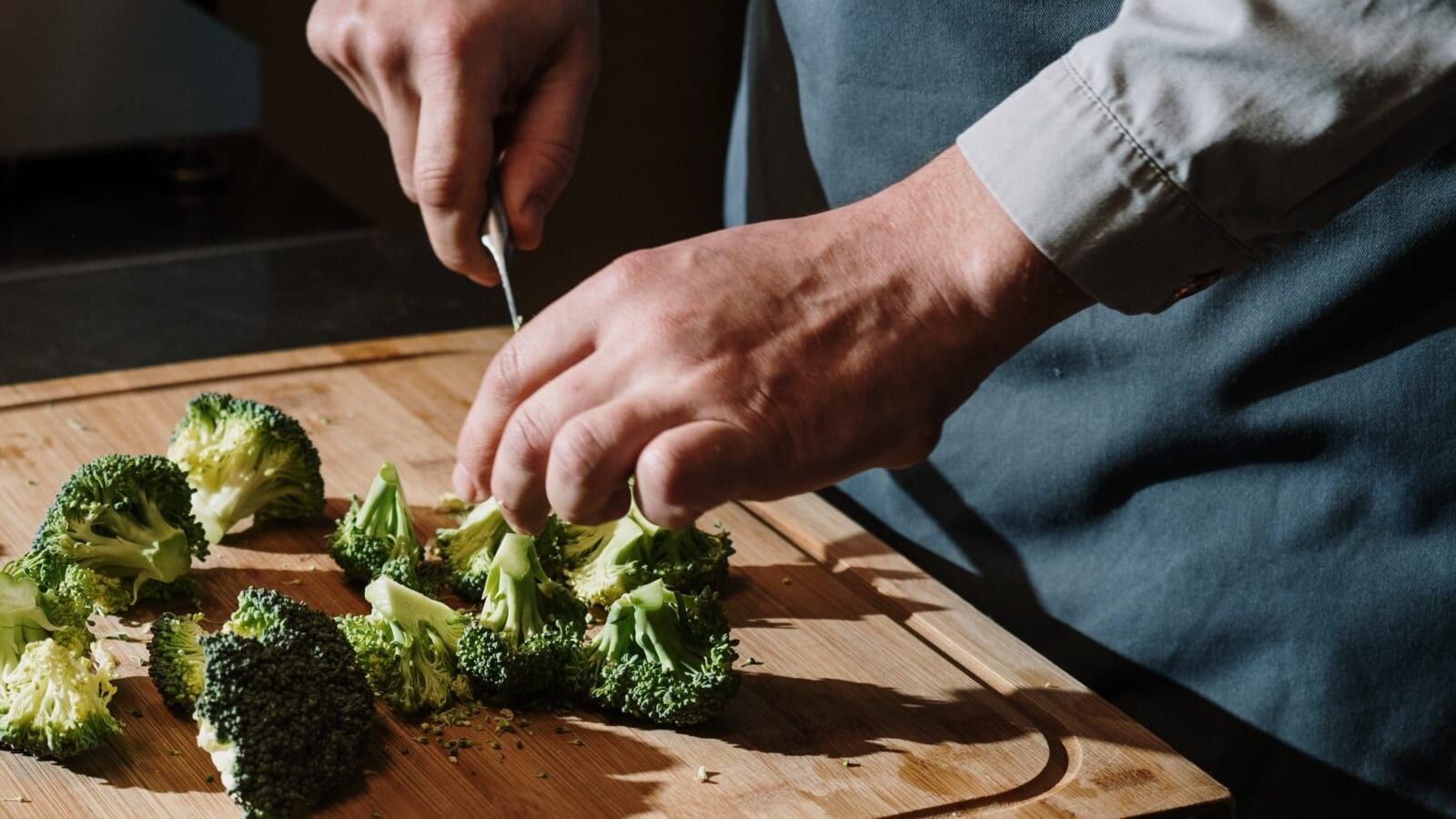 man chopping broccoli on a cutting board with a knife