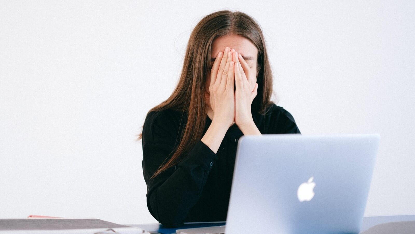 woman with her head in her hands in front of a laptop