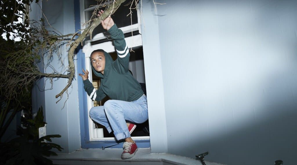 Full length of woman sneaking out of house window in yard