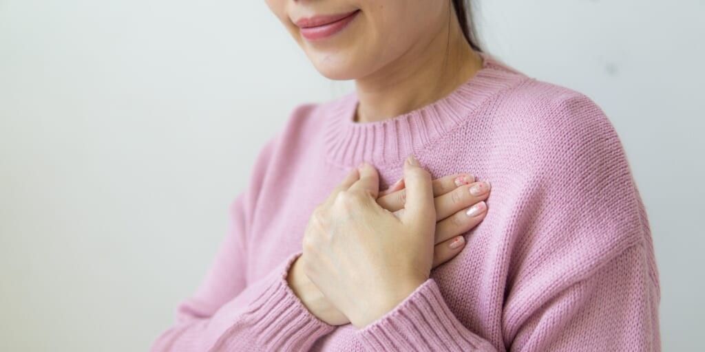 Smiling woman holding hands over heart by Puwadon Sangngern on Pexels