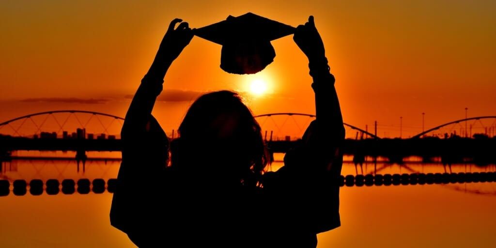 Silhouette of graduate holding cap up looking out at sunset by Joan Kwamboka on Unsplash