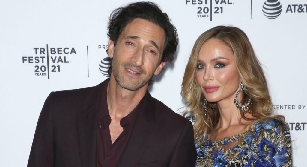Adrien Brody in black suit posing on red carpet with girlfriend Georgina Chapman.