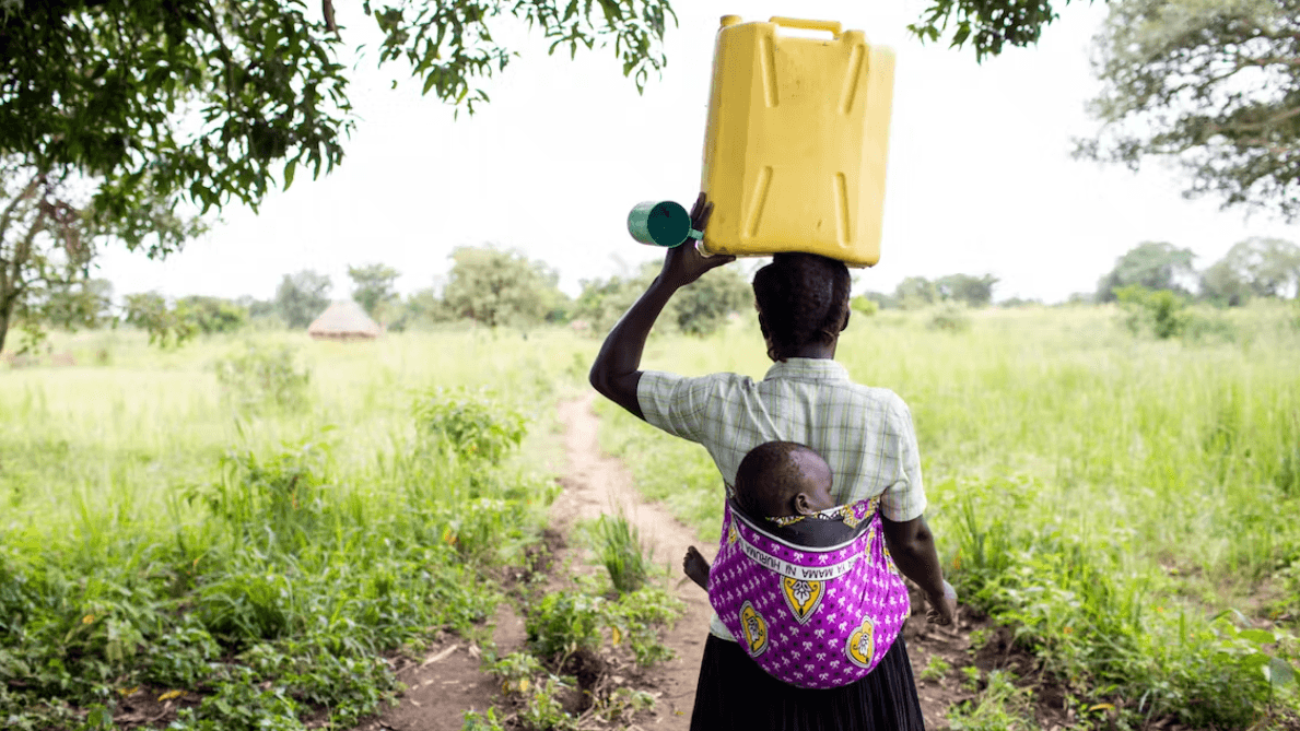 woman carrying a baby on her back and holding a yellow container on her head