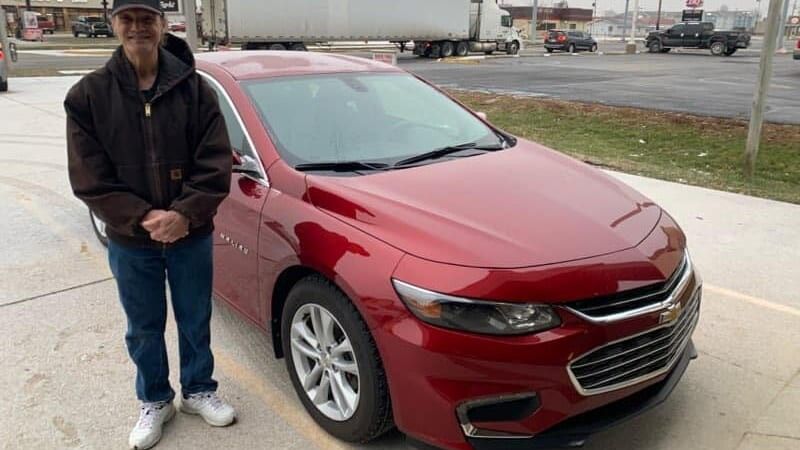 man stands next to a red car