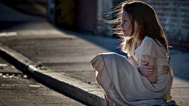 Little girl sitting on curb in dirty dress looking cold and alone