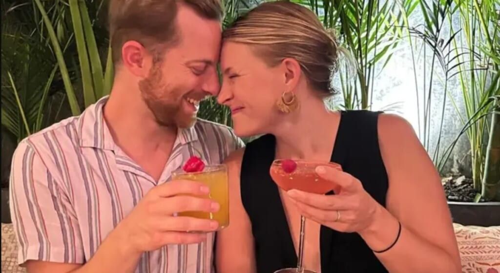 Video screenshot of Ned Fulmer and wife Ariel holding drinks with their heads close together.