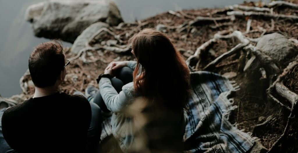 young man and woman have conversation seated in nature