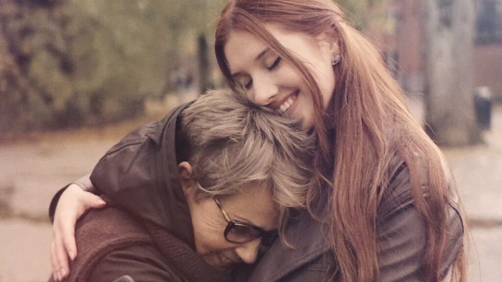 Red haired woman hugs her older mother in city park