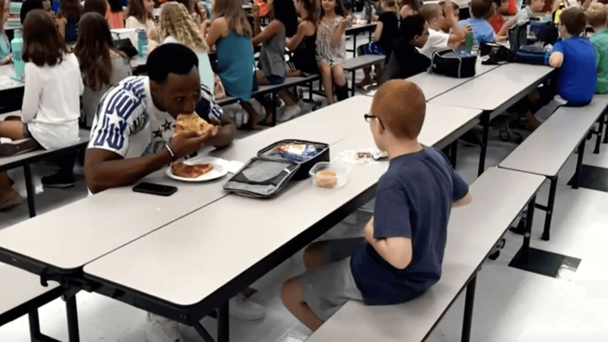 football player eating lunch with little boy at school