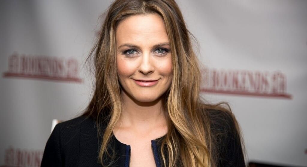 Alicia Silverstone smiling at the camera wearing a black dress.