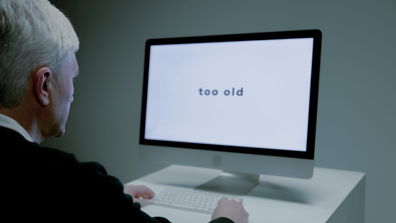 elderly man sitting in front of a computer with 