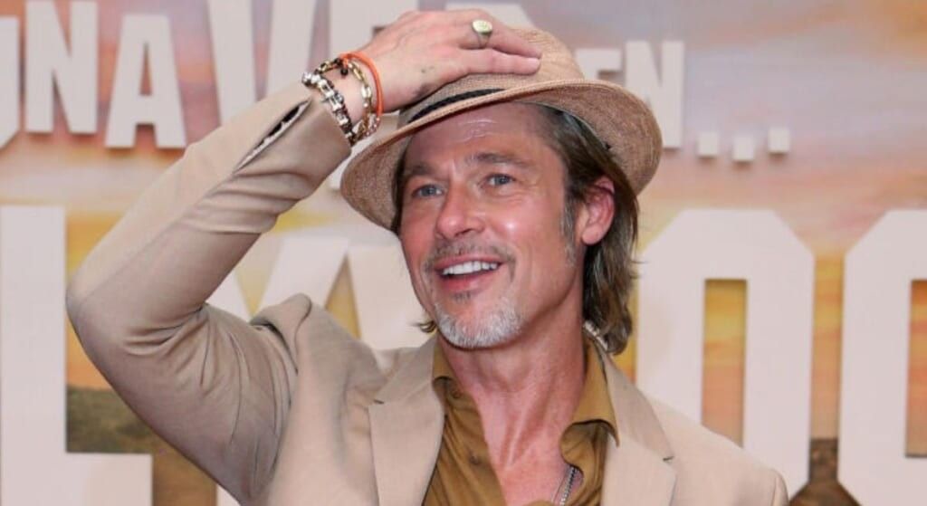 Brad Pitt with beige suit tipping his hat to the camera.