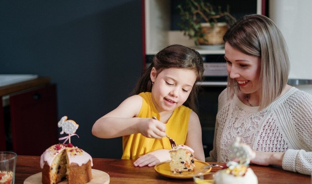 Mom and daughter eating cake on brown wooden table 3992140 1024x603