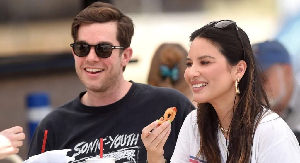 Olivia Munn and John Mulaney sitting at a picnic table and eating.