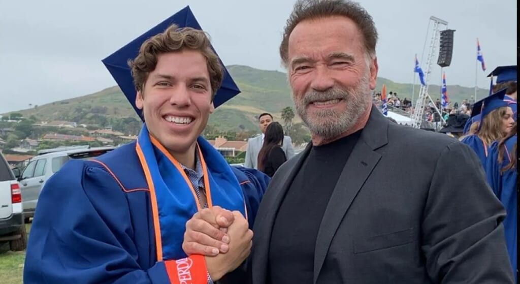 Joseph Baena wearing graduate cap and gown shaking his dad, Arnold  Schwarzenegger