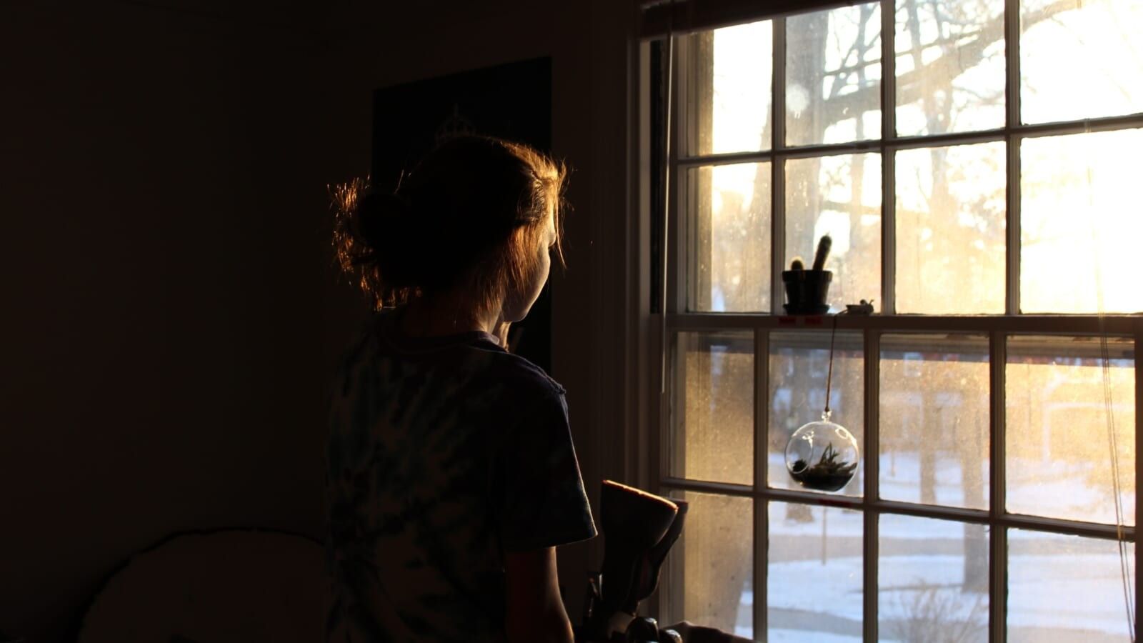 woman standing in a dark room in front of a bright window