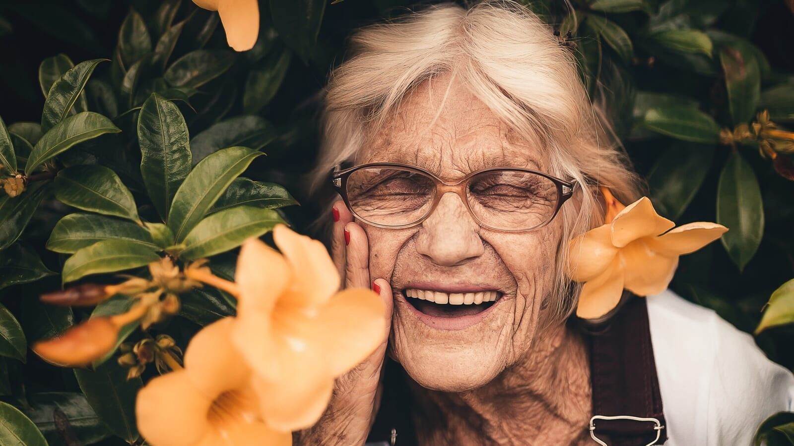 elderly woman smiling next to yellow flowers