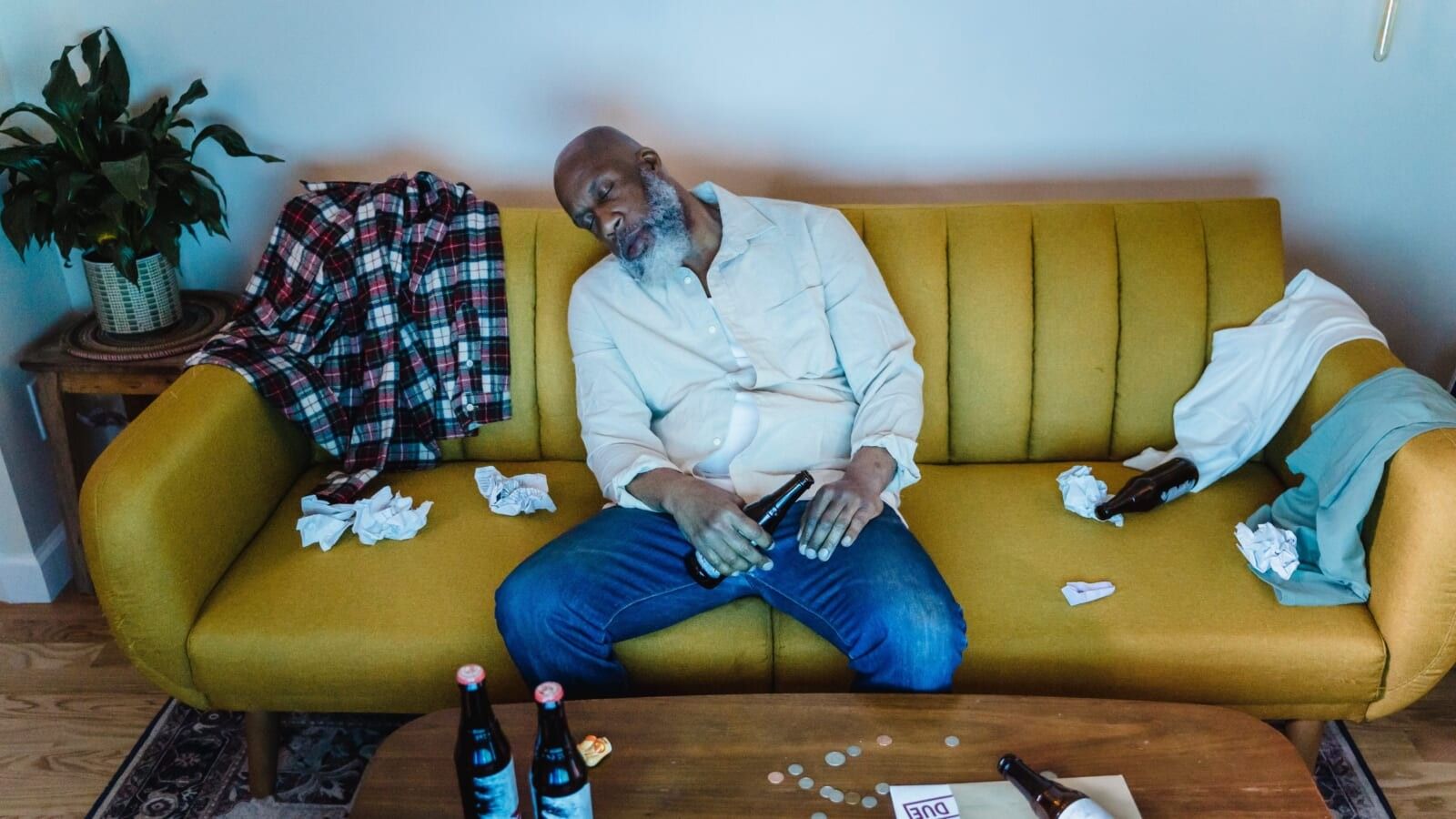 man wearing a white tshirt asleep on a messy couch