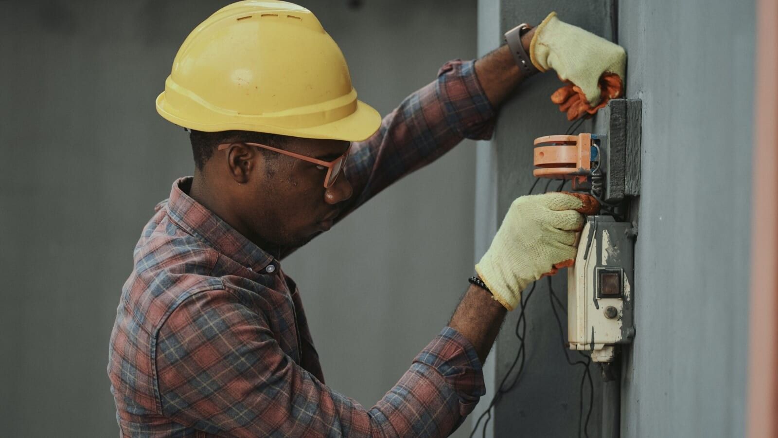 man with yellow hard hat drilling in the wall