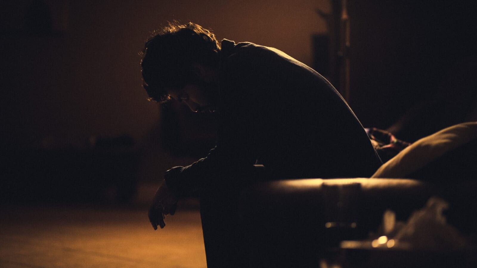 man sitting in the dark with head bent