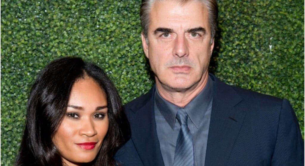 Chris Noth in black and grey suit posing with wife Tara Lynn Wilson on the red carpet.