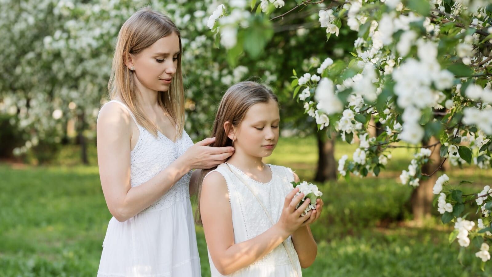 2 girls wearing white in a garden and older girl fixing younger girls hair