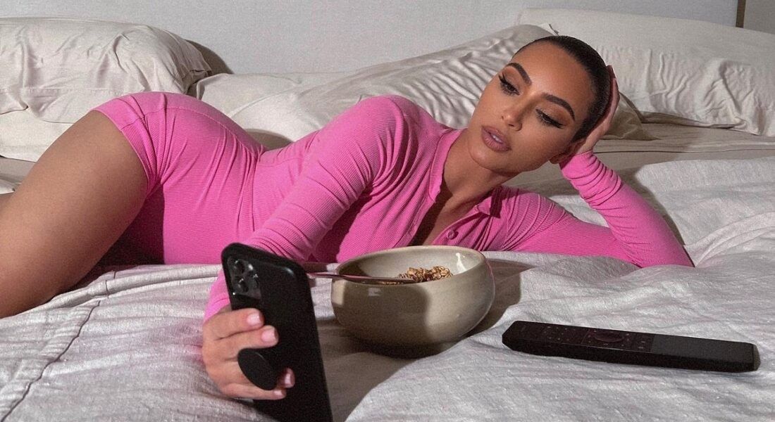 Kim Kardashian wearing all pink laying in bed and eating cereal.