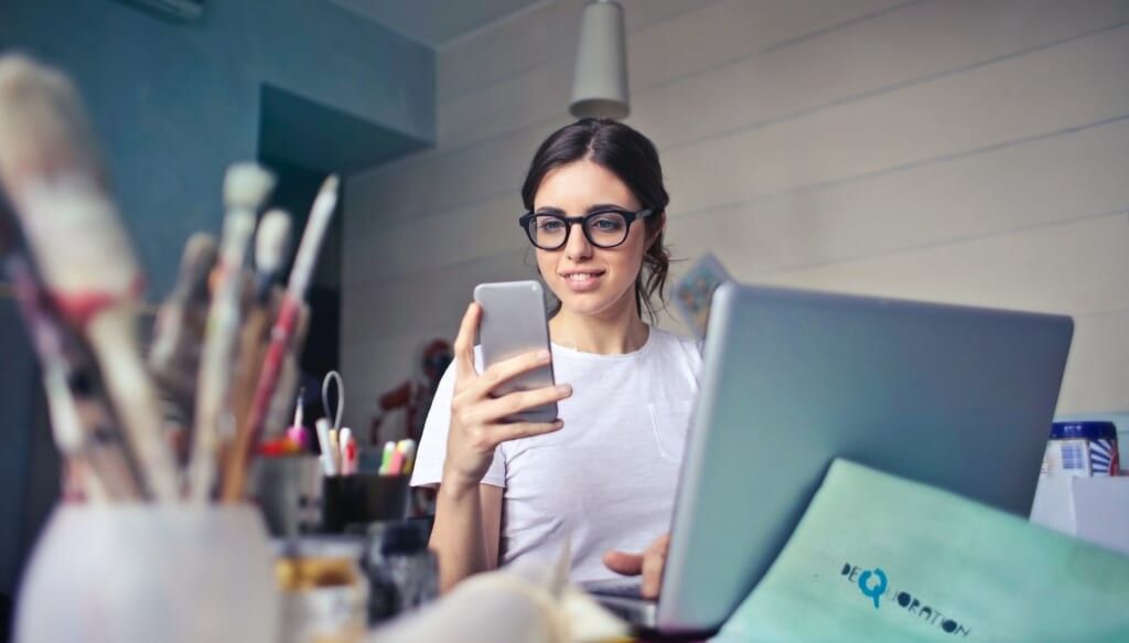 young woman checks her phone sitting at desk