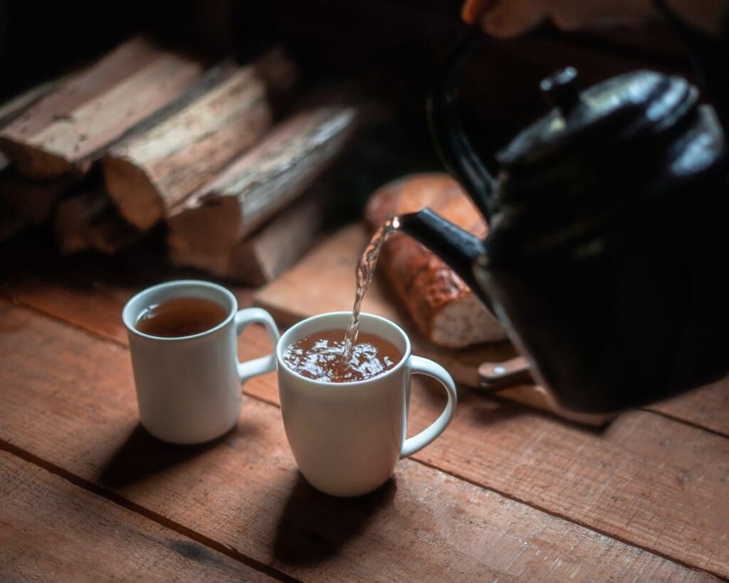 2 white cups of tea, kettle pouring tea into the cups