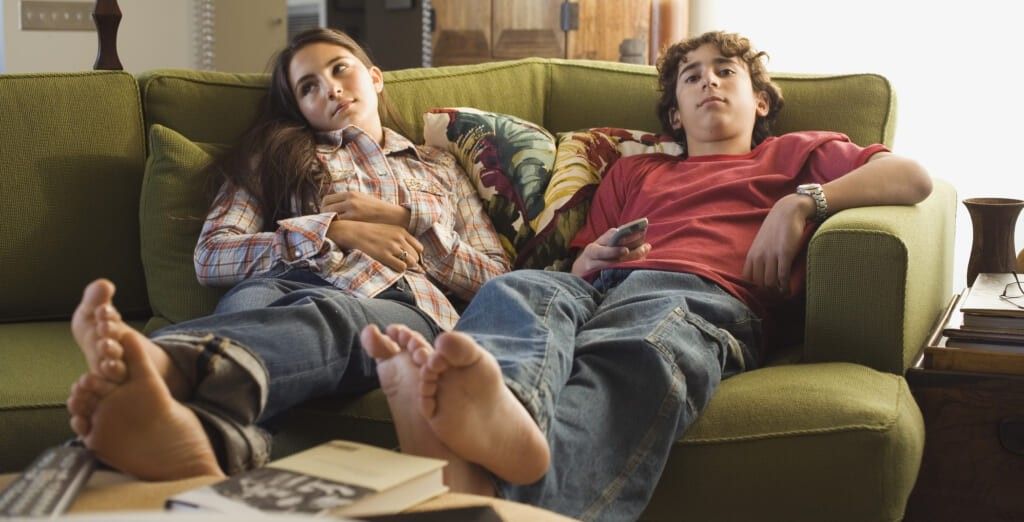 Boy and girl sitting on sofa with remote control