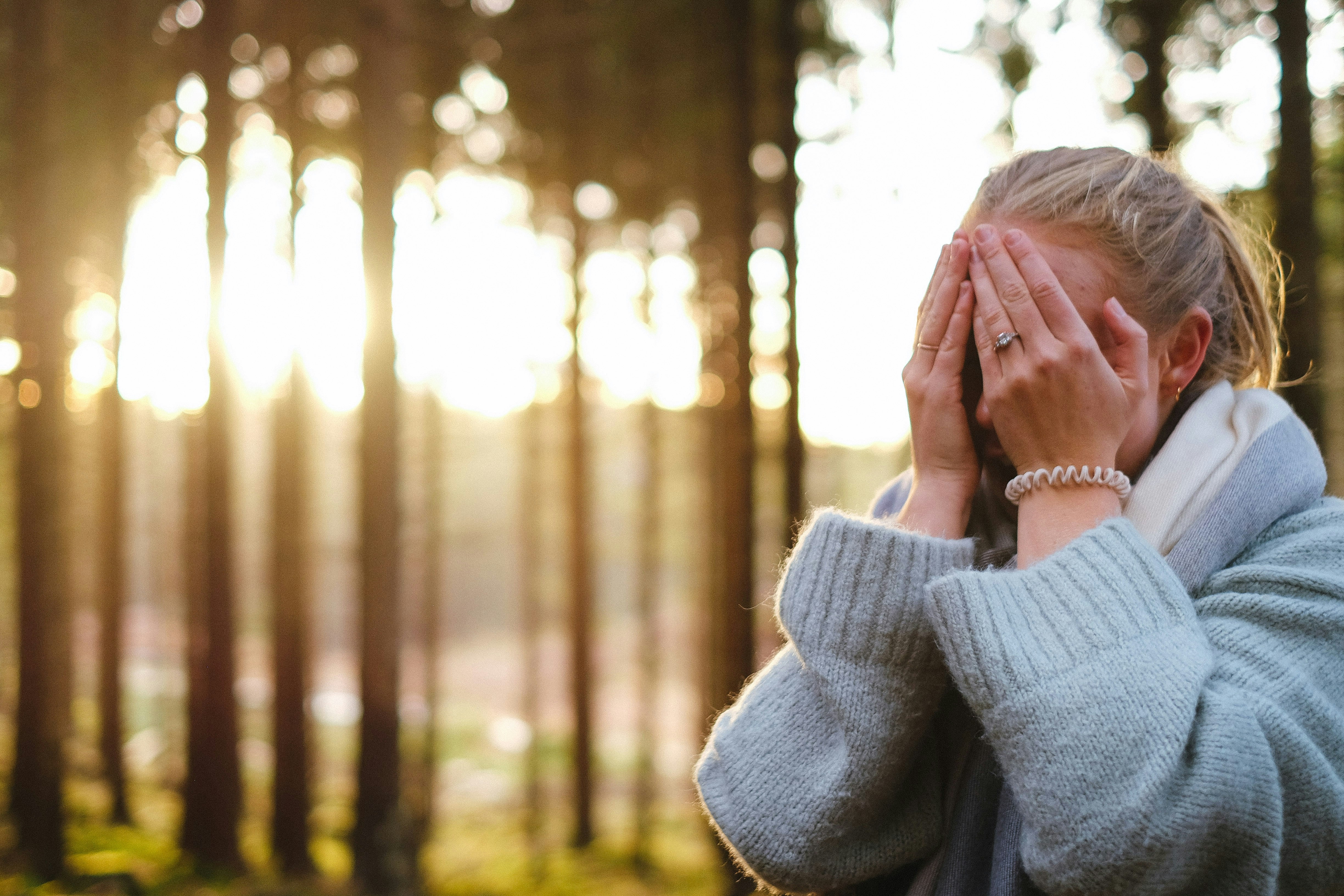 Woman wearing a gray outfit with her hands covering her face.